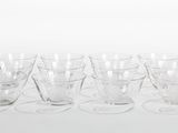 six clear glass cups and saucers sitting on a white surface