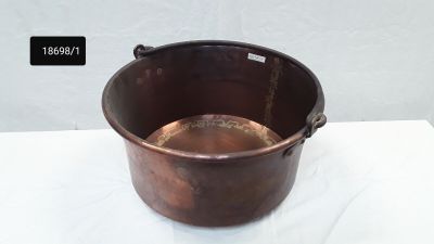 une grande casserole en cuivre avec une poignée, posée sur une table blanche