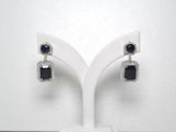 une paire de boucles d'oreilles en diamant noir et blanc posées sur un présentoir blanc
