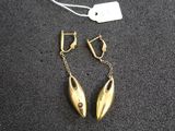 une paire de boucles d'oreilles en or posées sur une surface noire, avec une étiquette de prix