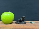 a green apple sitting next to a statue of a frog and a frog