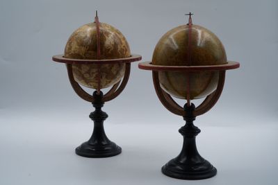 une paire de globes anciens posés sur des socles, sur fond blanc