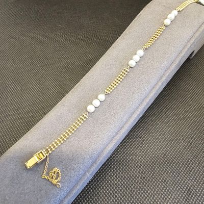 chaîne en or avec des perles et une clé, sur un écrin gris