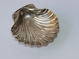 un objet argenté en forme de coquille posé sur une surface blanche