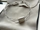 silver bracelet with a silver bar on it sitting on top of a bag