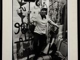 photographie en noir et blanc d'une femme debout devant un mur recouvert de graffitis