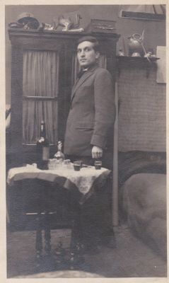 an old black and white photo of a man standing in front of a table with a bottle of wine on it