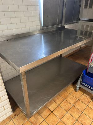 une table en acier inoxydable dans une cuisine, avec une poubelle posée par terre