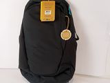 un sac à dos noir muni d'une étiquette, posé contre un mur