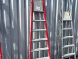 Plusieurs échelles sont alignées contre un mur métallique devant un immeuble.