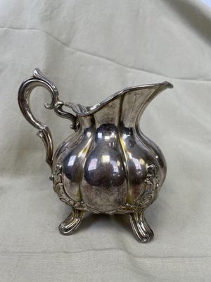 un pichet ancien plaqué argent posé sur une nappe blanche