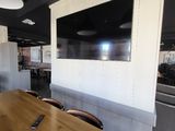 des tables et des chaises dans une pièce où est accrochée une télévision à écran plat au mur
