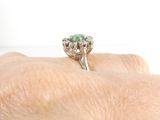 a woman ' s hand holding a diamond and emerald ring