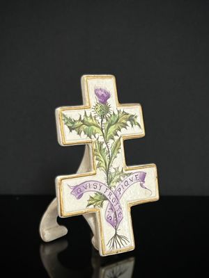 une croix ornée d'un chardon et d'un ruban, posée sur une surface noire
