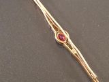a gold tie bar with a red stone on it