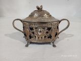 une théière ancienne en métal plaqué argent, avec un couvercle, posée sur une surface blanche