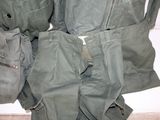 a pile of military pants and backpacks on a bed