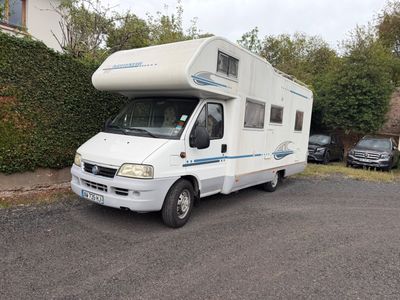 un camping-car blanc garé sur un parking à côté d'une maison