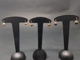 trois paires de boucles d'oreilles posées sur un présentoir noir, sur fond gris