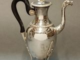 a silver tea pot with a black handle on a stand