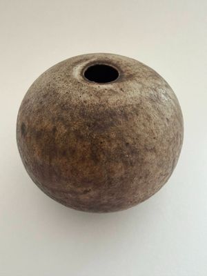 un vase marron percé d'un trou, posé sur une surface blanche