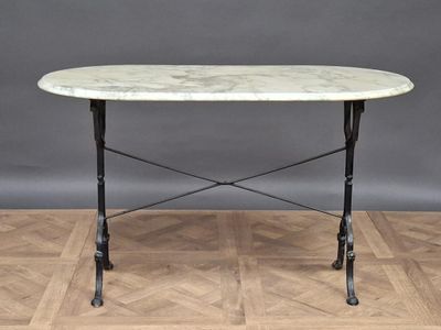 an oval marble table with iron legs on a parquet wood floor