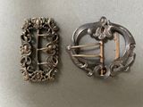 two antique silver buckles on a table next to each other