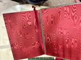 a person holding a red book open on a table