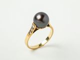 une bague en perle noire et diamants sur fond blanc