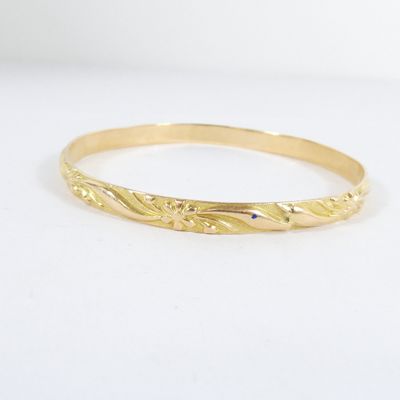 un gros plan sur un bracelet rigide en or jaune au motif ondulé