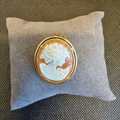 une broche en camée dorée et blanche posée sur un coussin