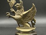 statue en laiton représentant un oiseau tenant un drapeau, posée sur un socle
