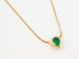 a close up of a gold necklace with a green heart on it