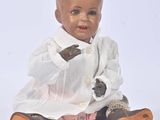 a baby doll sitting on the ground wearing a white shirt