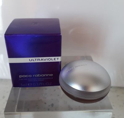 un flacon de parfum et son coffret posés sur un plan de travail, près d'un mur blanc