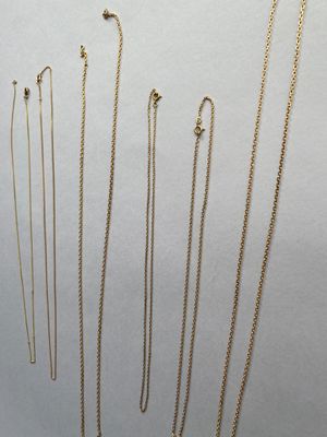 Plusieurs colliers en or sont disposés en rangée sur une surface blanche