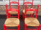 four red chairs with wicker seats in front of a house