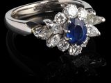 une photo d'une bague en saphir et diamants posée sur un fond noir