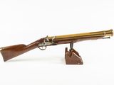 un pistolet ancien plaqué laiton, posé sur un socle en bois, sur fond blanc