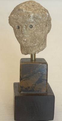 sculpture représentant un rocher avec un visage, posée sur un bloc de bois