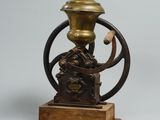 un moulin à café ancien monté sur un socle en bois et muni d'une poignée en métal