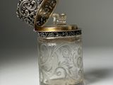 an antique silver and glass jar with a lid on a white surface