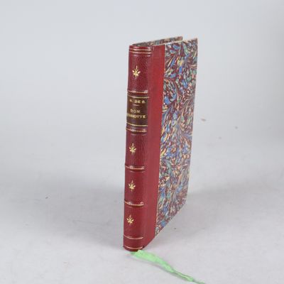 un vieux livre rouge posé sur une table, à côté d'un ruban vert