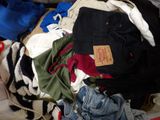 a pile of clothes on a bed with a pair of scissors