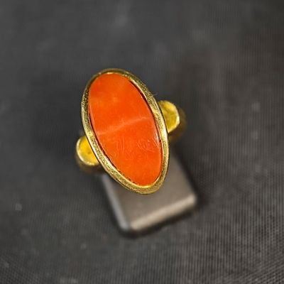 une image représentant une bague ornée d'une pierre orange posée sur un support en métal