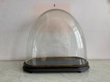 une cloche en verre avec un socle noir posée sur une table