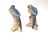 two figurines of parrots sitting on a tree stump