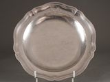 un plat en argent ancien posé sur un support, sur fond gris