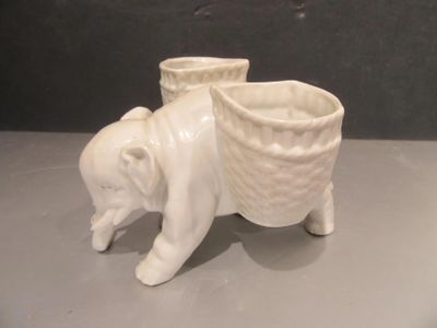 a white ceramic elephant with a basket on it ' s back