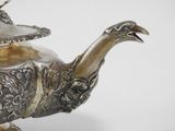 a silver teapot with a lid and a bird on it